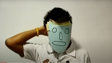 A teenage boy removes a mask showing his emotions from his face.