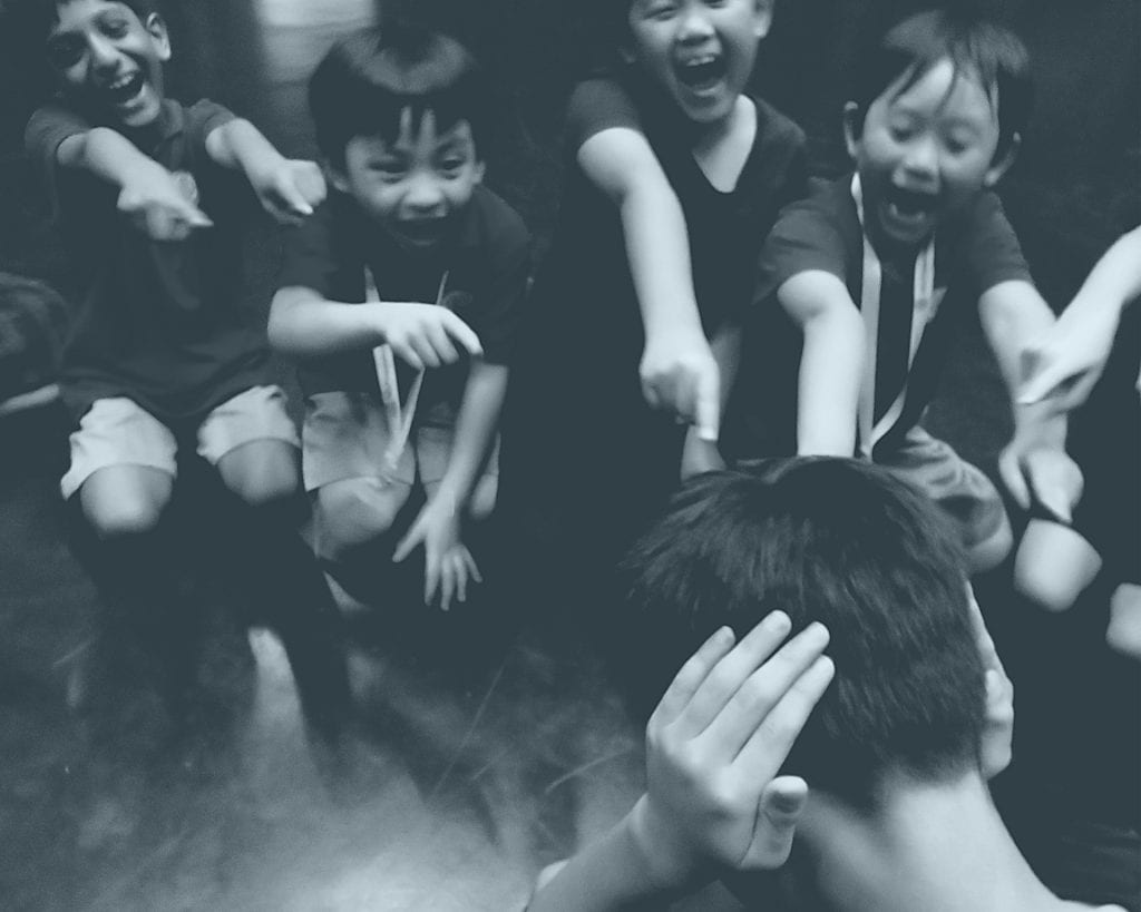 a group of children are pointing fingers at another child who has closed his ears with his hands.