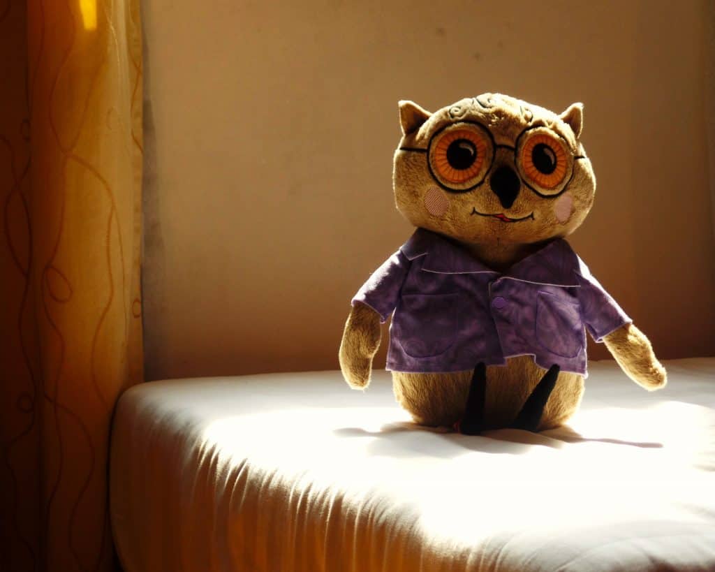 a soft toy owl stands on a bed.