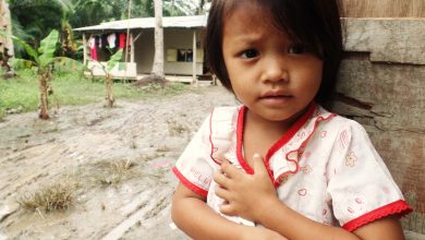 An orang Asli child stands outside her wooden house.