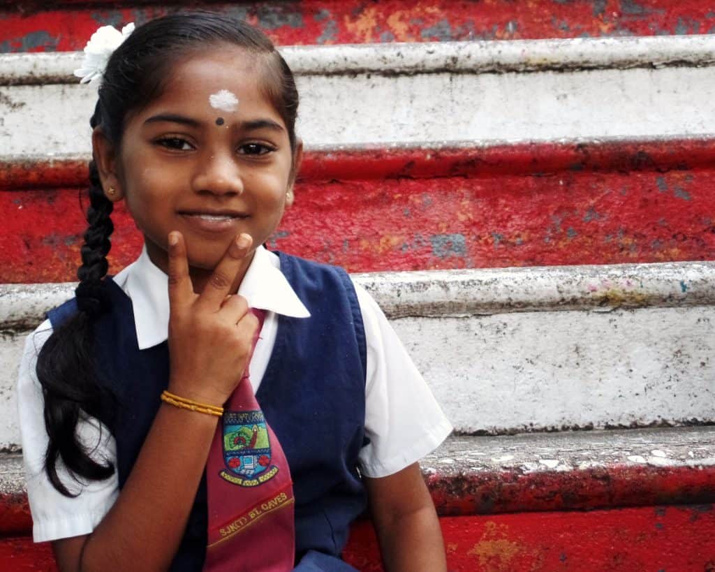 An Indian primary school girl sits on stairs holding up a peace sign.