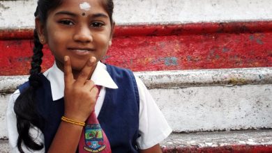 An Indian primary school girl sits on stairs holding up a peace sign.