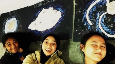 Three girls stand in front of a black board.