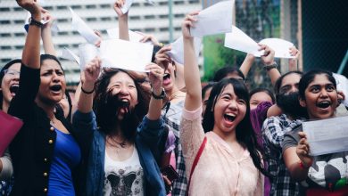 a group of girls hold up their exam results. The girls are smiling and laughing.