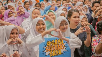 a group of school students showing the heart sign with their two hands as a symbol calling for sex education to protect them.. Two girls hold a sign board with the words Saya Sayang Saya.