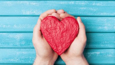 An paper mache designed in the shape of a heart is cradled in the palms of two hands..