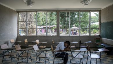 a boy who is a victim of violence sits alone in his empty classroom. He has his head on the table.