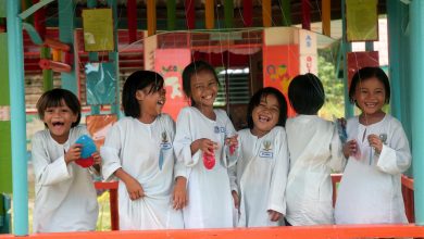 six primary school girls stand in a row outside their classroom. They are smiling and look happy.