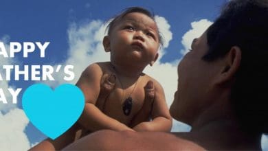 A father holds up his infant son. Next to him are the words Happy Father's Day.