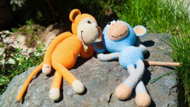 Two stuffed toy monkeys, one orange, one blue, basking under the sun in the garden.