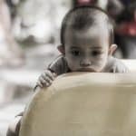 A sad looking child rests in chin on the bottom of a slide.