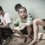 a group of boys eating. One boy looks up with sad face.