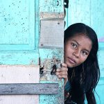 a teenage girl peers from behind a door.