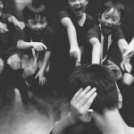 a group of young boys point towards another boy who closes his ears with both hands.