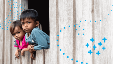 Two migrant children in Malaysia - a girl and a boy - look out of window of a wooden house.